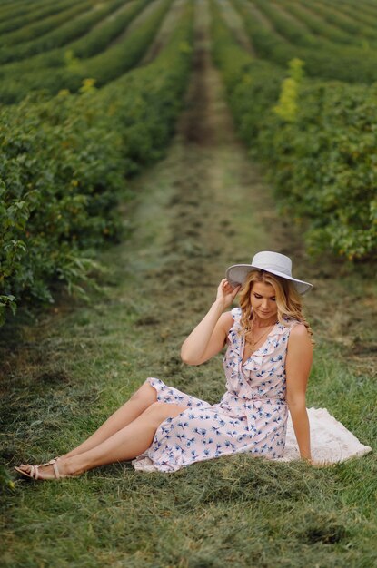 Giovane donna alla moda in vestito e cappello dall'annata blu rosa che posa nel campo verde