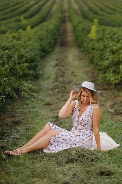 Giovane donna alla moda in vestito e cappello dall'annata blu rosa che posa nel campo verde