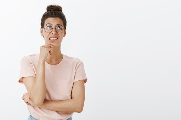 Giovane donna alla moda indecisa e preoccupata che posa contro il muro bianco