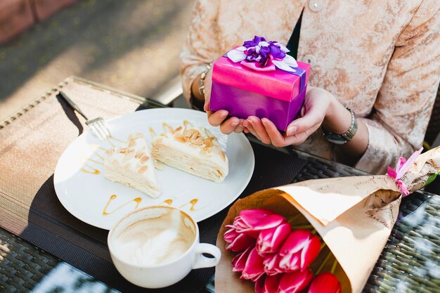 Giovane donna alla moda, seduta al caffè, tenendo presente la casella