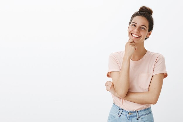 Giovane donna alla moda spensierata che posa contro il muro bianco