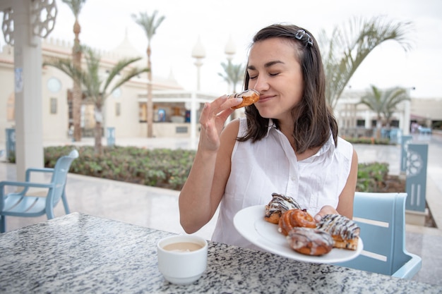 Giovane donna allegra che gode del caffè del mattino con ciambelle sulla terrazza all'aperto