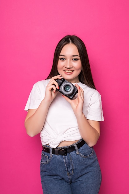 Giovane donna allegra con la macchina fotografica sulla parete rosa