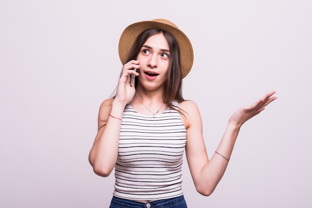 Giovane donna allegra in cappello che parla sul telefono cellulare isolato su un fondo grigio