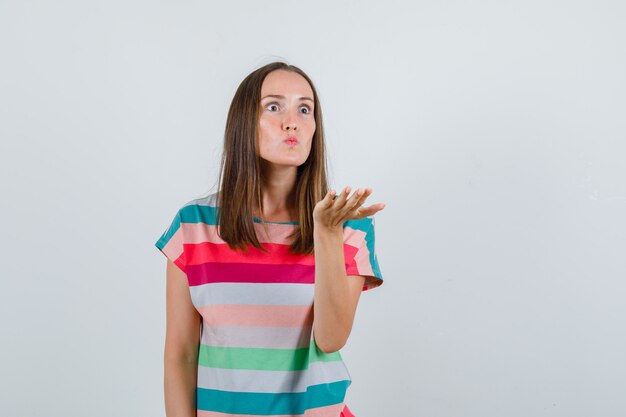 Giovane donna alzando la mano in modo aggressivo in maglietta e guardando arrabbiato, vista frontale.