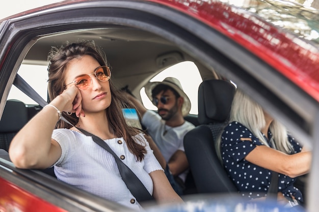 Giovane donna annoiata che viaggia in automobile moderna con i suoi amici