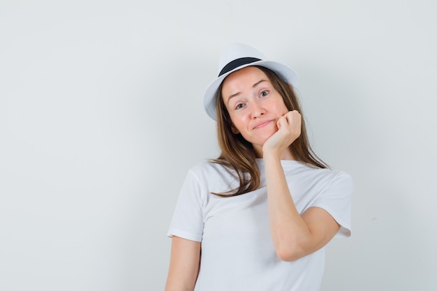 Giovane donna appoggiando il mento sul palmo in cappello bianco della maglietta e guardando pensieroso