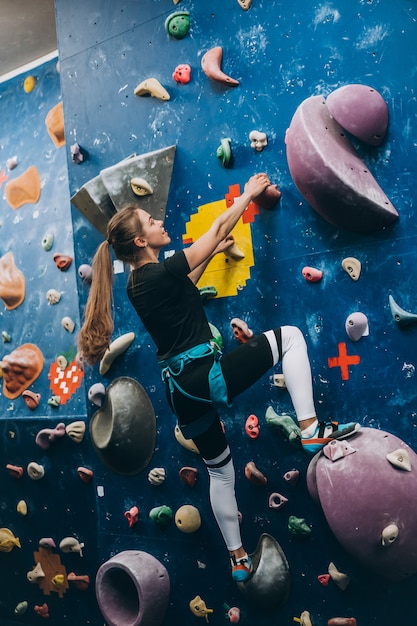 Giovane donna arrampicata su una parete di arrampicata alta, coperta, artificiale