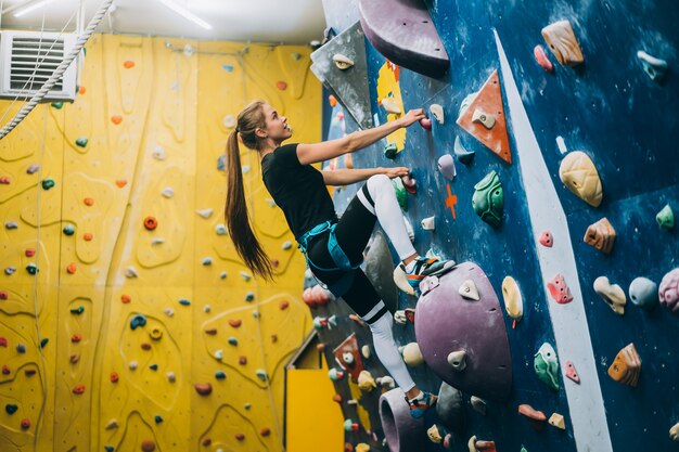 Giovane donna arrampicata su una parete di arrampicata su roccia alta, coperta, artificiale