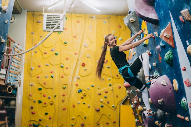 Giovane donna arrampicata su una parete di arrampicata su roccia alta, coperta, artificiale