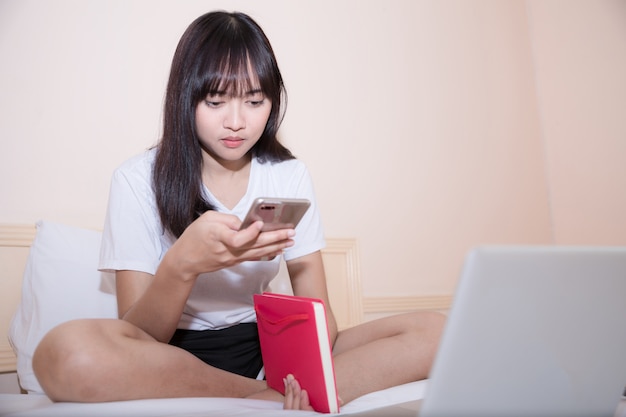 Giovane donna asiatica attraente che per mezzo del computer portatile mentre trovandosi sul letto in abbigliamento casual