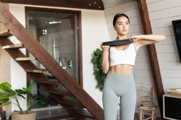 Giovane donna asiatica che fa allenamento fitness a casa con fascia elastica per allungare la corda per sta...
