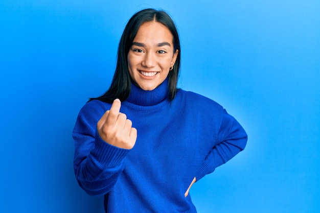 Giovane donna asiatica che indossa un maglione invernale casual che fa cenno di venire qui gesto con la mano che invita ad accogliere felice e sorridente