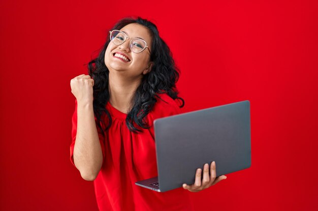 Giovane donna asiatica che lavora utilizzando il computer portatile del computer che celebra la vittoria con il sorriso felice e l'espressione del vincitore con le mani alzate