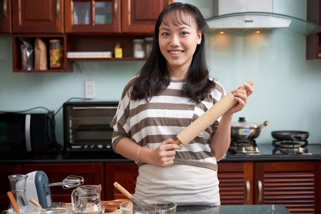 Giovane donna asiatica che posa nella cucina a casa con gli utensili di cottura