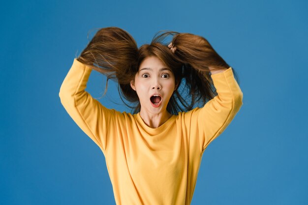 Giovane donna asiatica che sente felicità con l'espressione positiva, funky gioiosa sorpresa, vestita in un panno casual e guardando la telecamera isolata su sfondo blu. La donna felice adorabile felice si rallegra del successo