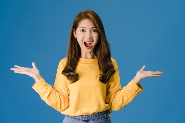 Giovane donna asiatica che sente felicità con l'espressione positiva, funky gioiosa sorpresa, vestita in un panno casual e guardando la telecamera isolata su sfondo blu. La donna felice adorabile felice si rallegra del successo