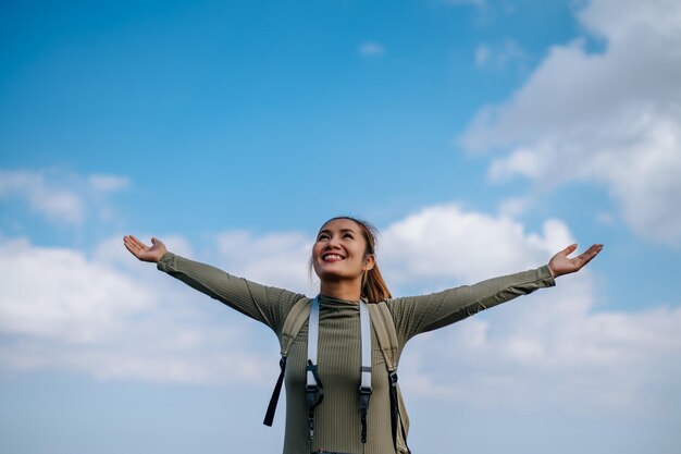 Giovane donna asiatica che sta in piedi e si alza le mani con un sorriso felice e fresca sul picco della montagna rocciosa Nuvoloso sopra la valle sullo spazio della copia del fondo