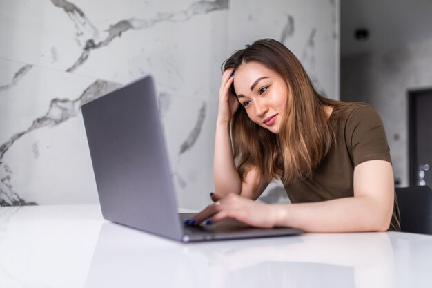 Giovane donna asiatica che utilizza il computer portatile in cucina