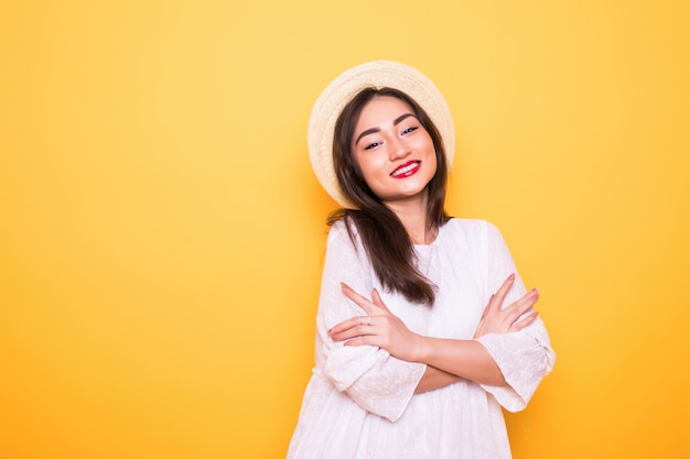 Giovane donna asiatica con il cappello di paglia isolato sulla parete gialla