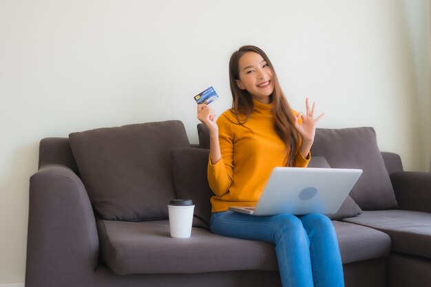 Giovane donna asiatica del ritratto che per mezzo del computer portatile con il telefono cellulare e la carta di credito astuti per acquisto online