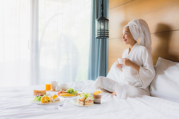 Giovane donna asiatica del ritratto sul letto con la prima colazione in camera da letto