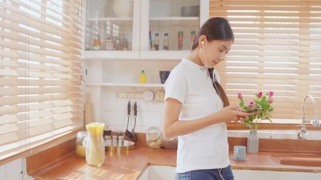 Giovane donna asiatica dell&#39;adolescente che beve caffè caldo facendo uso di musica d&#39;ascolto dello smartphone e controllando sociale