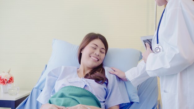 Giovane donna asiatica di medico che parla e che tiene mano per le donne paziente nel letto malato.