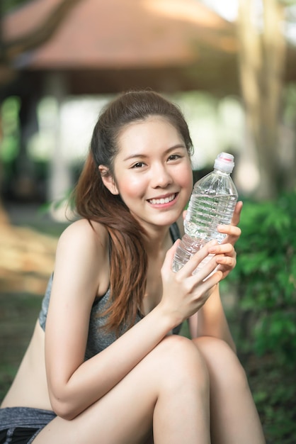 Giovane donna asiatica di sport che beve acqua durante l'allenamento nel concetto di stile di vita e sano all'aperto del parco