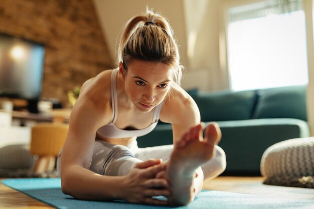 Giovane donna atletica che fa esercizi di stretching sul pavimento a casa