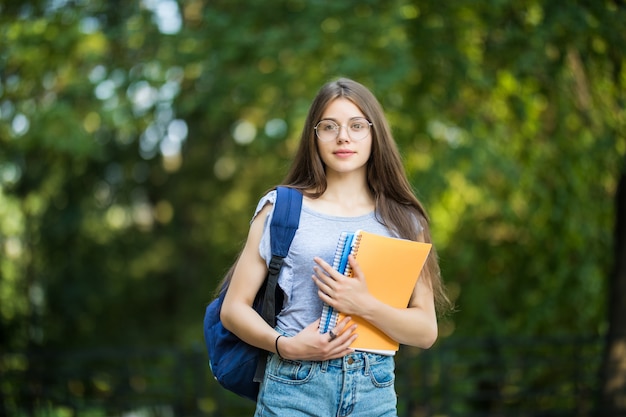 Giovane donna attraente allegra con zaino e notebook in piedi e sorridente nel parco