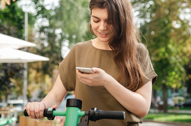 Giovane donna attraente con uno scooter elettrico a noleggio in una giornata di sole