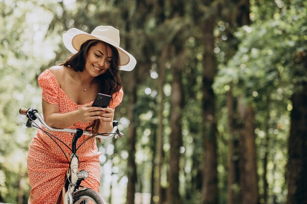 Giovane donna attraente in bicicletta da equitazione vestito e utilizzando il telefono