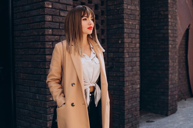 Giovane donna attraente in cappotto beige in posa in strada