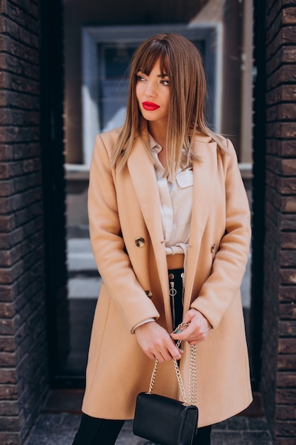 Giovane donna attraente in cappotto beige in posa in strada