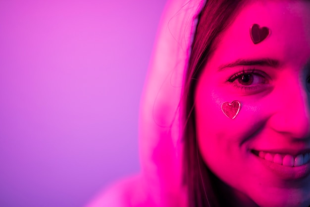 Giovane donna attraente sorridente in cappuccio con i cuori sul viso