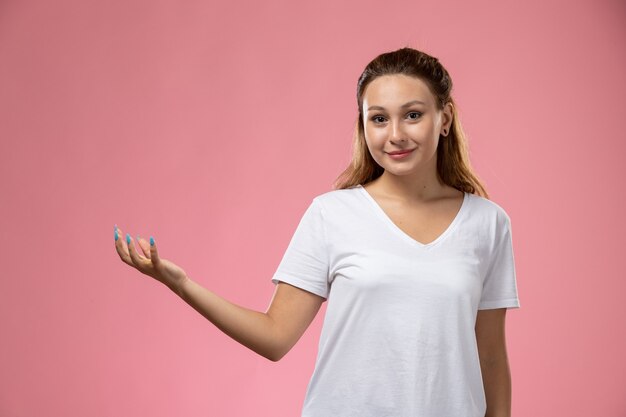 Giovane donna attraente vista frontale in maglietta bianca in posa con un leggero sorriso su sfondo rosa