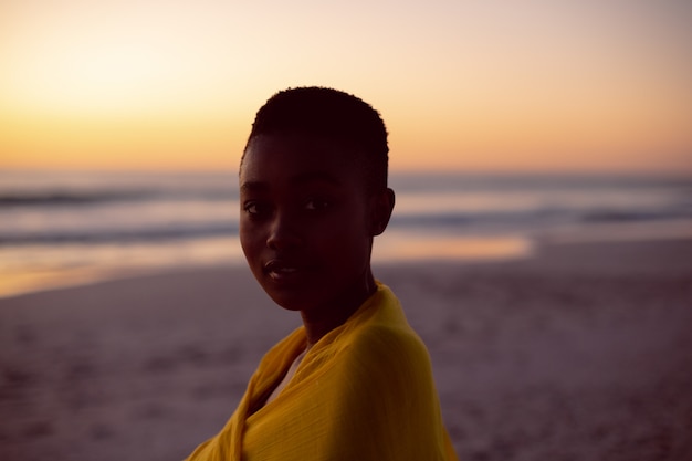 Giovane donna avvolta in sciarpa gialla sulla spiaggia