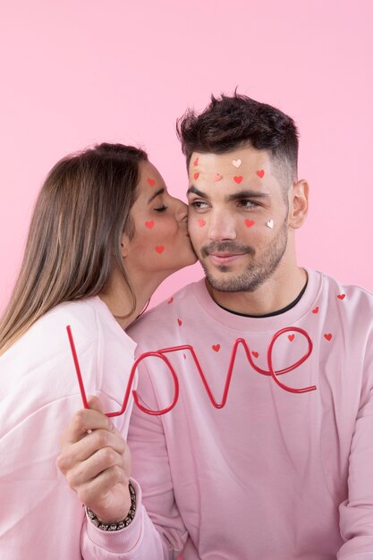 Giovane donna bacia il ragazzo con cuori di carta sui volti e segno di amore