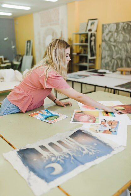 Giovane donna bionda che esamina le pitture sul banco da lavoro