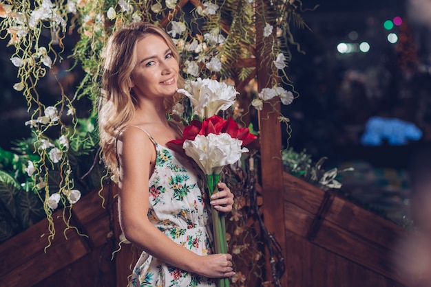 Giovane donna bionda che esamina macchina fotografica che tiene fiore rosso e bianco a disposizione