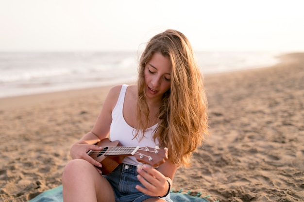 Giovane donna bionda che gioca ukulele alla spiaggia