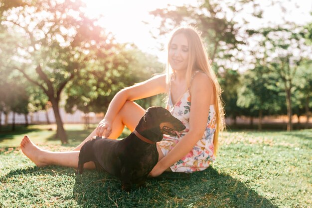 Giovane donna bionda che si siede con il suo cane al parco