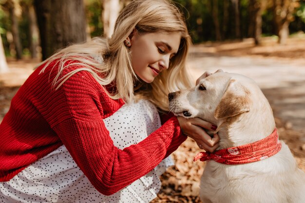 Giovane donna bionda che sorride al suo cane. Bella ragazza che condivide bei momenti con un animale domestico nel parco.