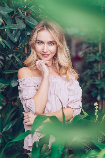 Giovane donna bionda che sta nel giardino che esamina macchina fotografica