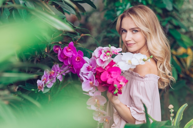 Giovane donna bionda che sta nell&#39;orchidea della tenuta del giardino