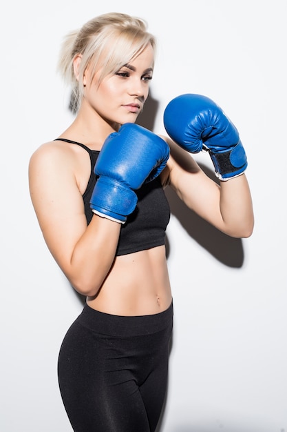 Giovane donna bionda con guantoni da boxe blu pronti a combattere su bianco