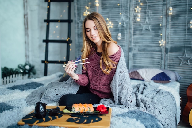 Giovane donna bionda e riccia che mangia sushi a casa