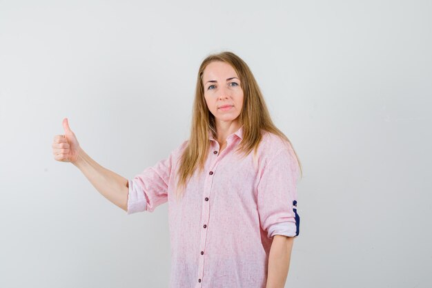 Giovane donna bionda in una camicia rosa casual che mostra i pollici in su