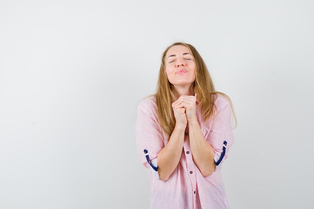 Giovane donna bionda in una camicia rosa casual che prega